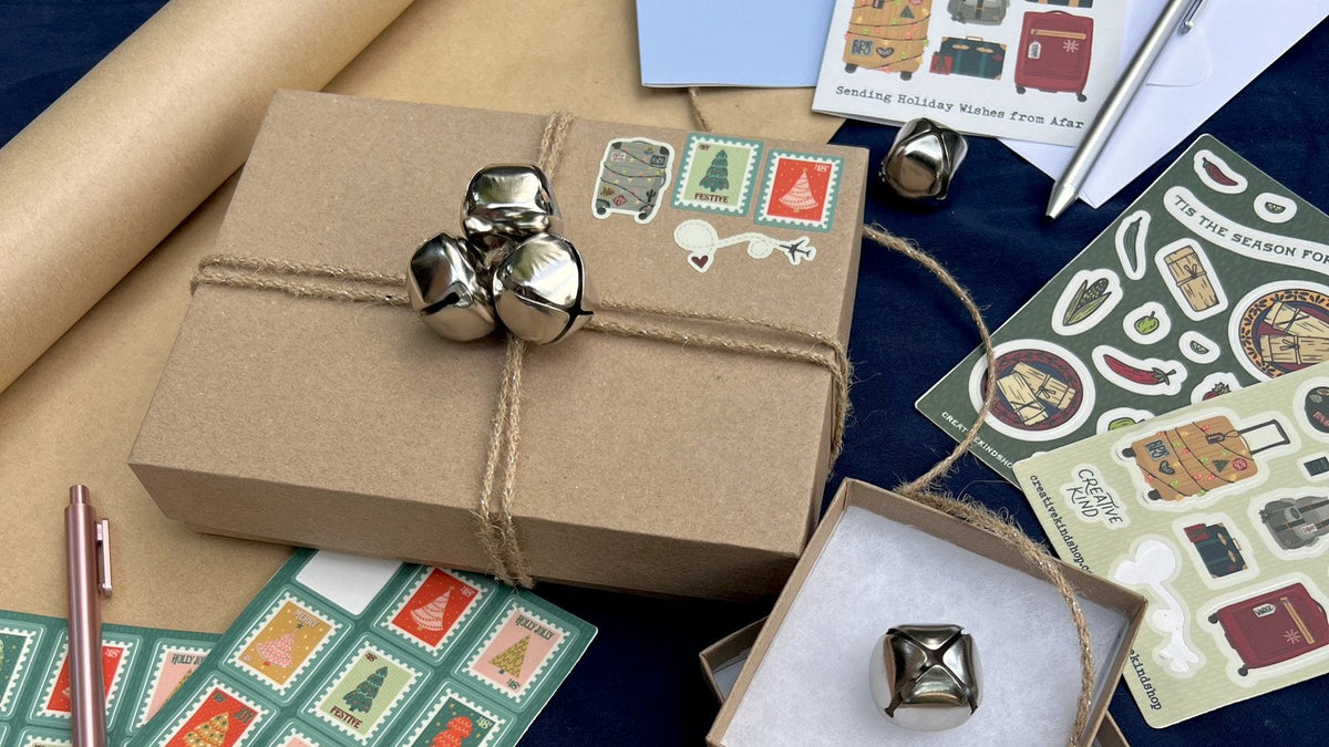 Kraft gift box tied with twine and jingle bells, with holiday stamp sticker sheets and greeting cards