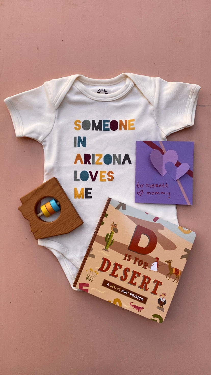 Photo layout from instagram featuring a onesie, a wooden rattle, d is for desert book, and a card that reads "to everett love mommy"