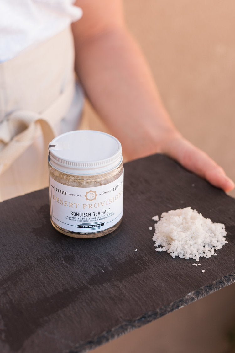 Person holding a tray with a jar of sonoran sea salt next to a pile of the salt to show texture