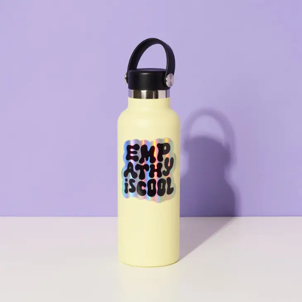 Yellow water bottle in front of a purple background with a holographic empathy is cool vinyl sticker