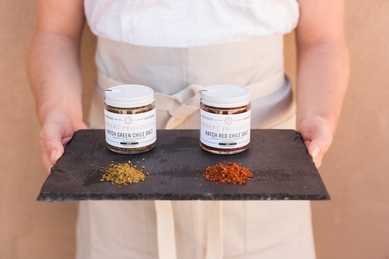 Person holding a tray with hatch green chile salt and hatch red chile salt behind piles of each salt used to show texture