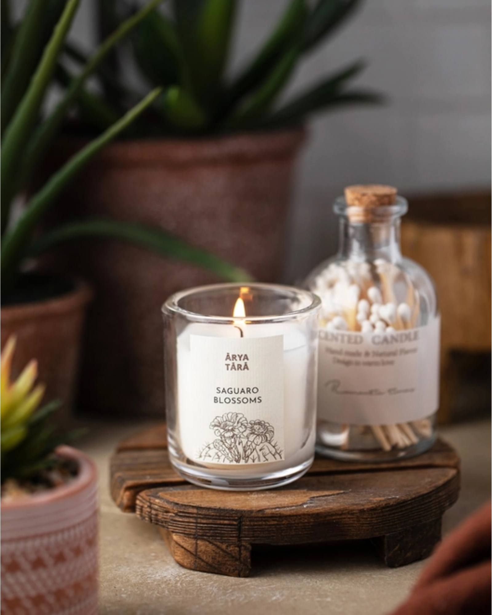 Lit saguaro blossom candle on a wood pedestal in front of a jar of candles