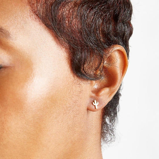 Person wearing gold saguaro cactus stud earrings